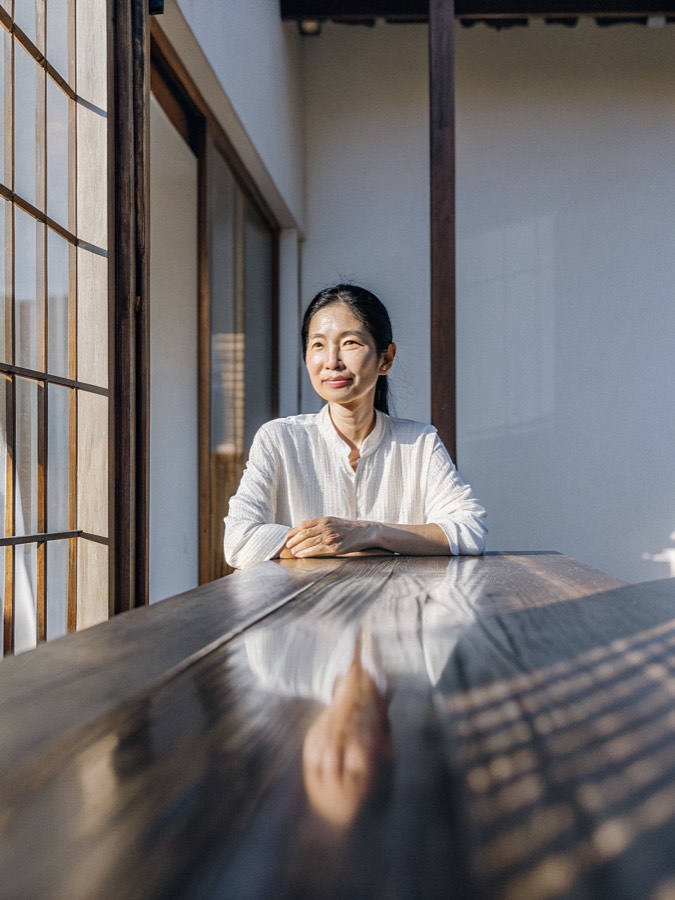 a Vietnamese woman in her mid fifties seated at a wooden table in warm afternoon light