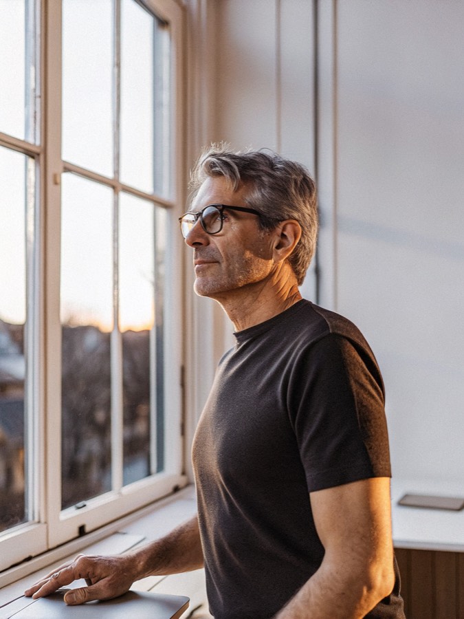 a white man in his late forties at a standing desk by a window at dusk