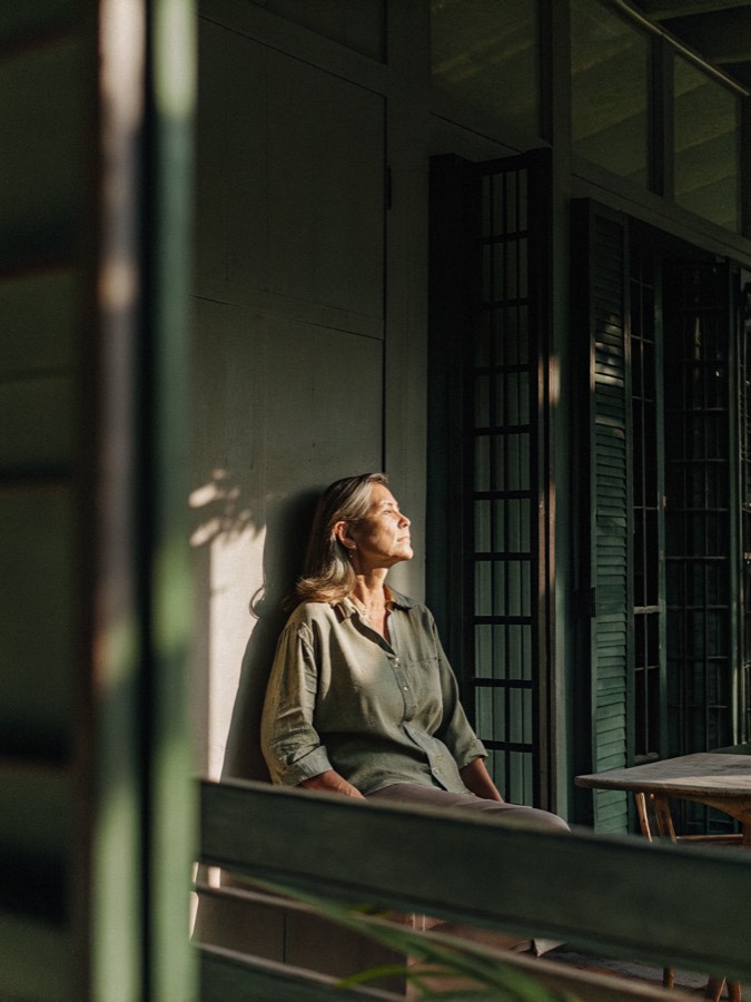 a white woman in her late forties resting on a shaded verandah in warm morning light