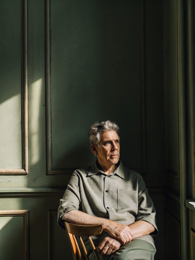a white man in his mid sixties seated in a quiet room in warm early light